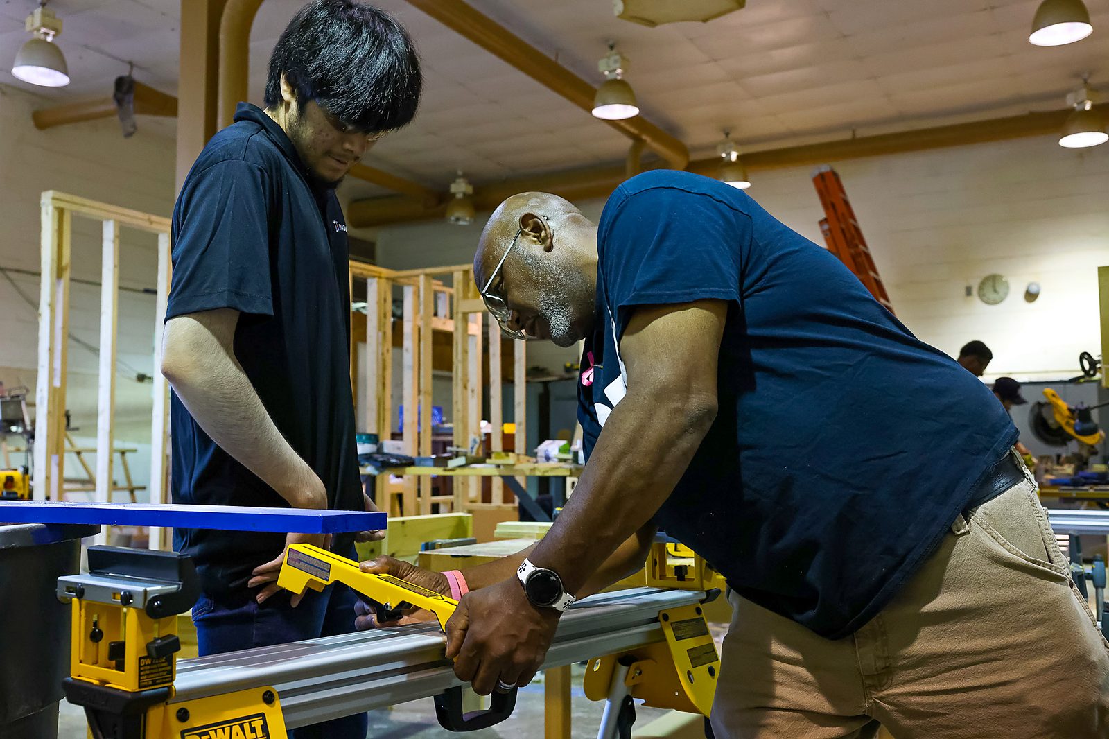 A tradesperson guiding a student at a saw station