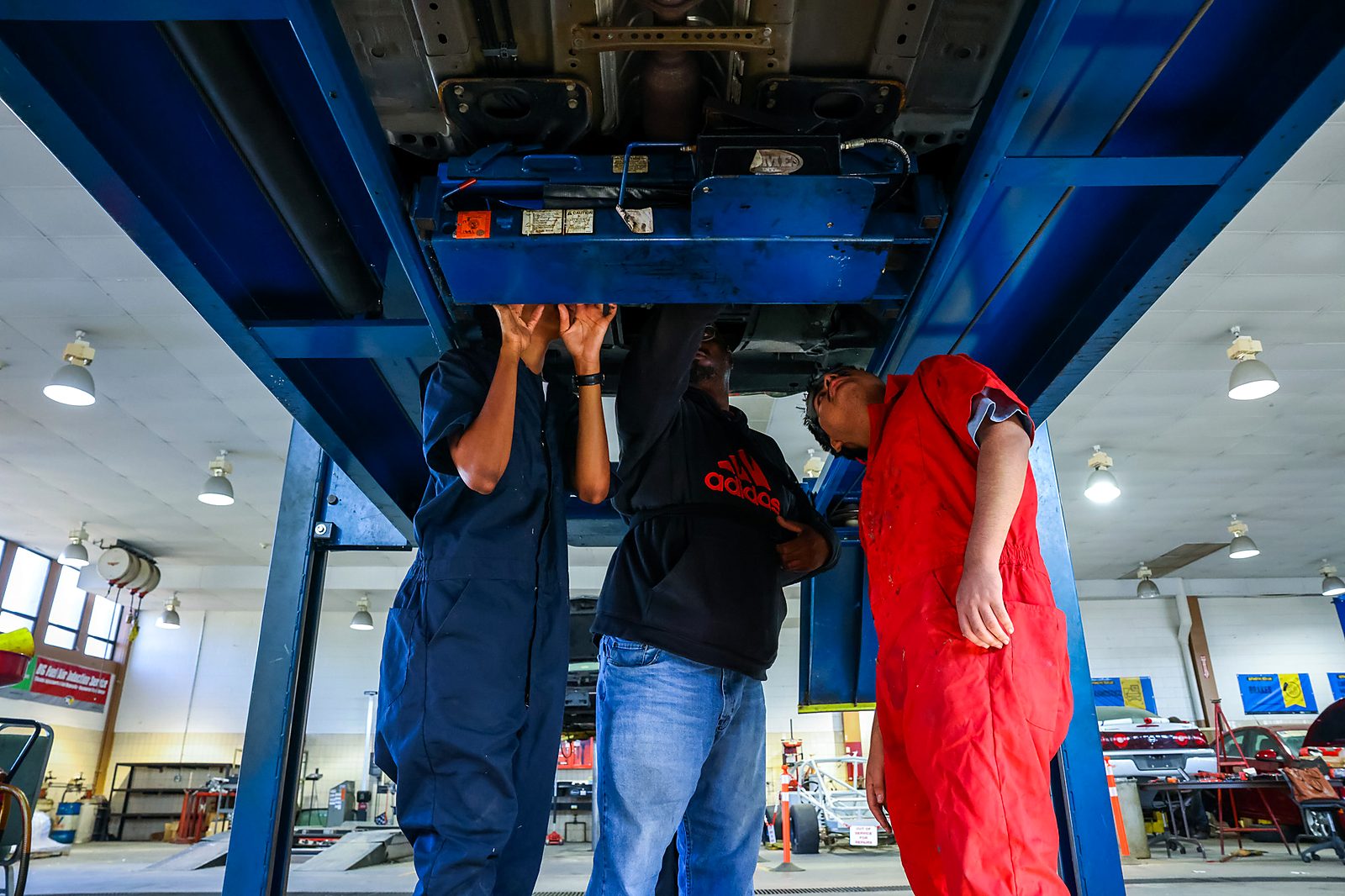 An instructor and students working under a car lift